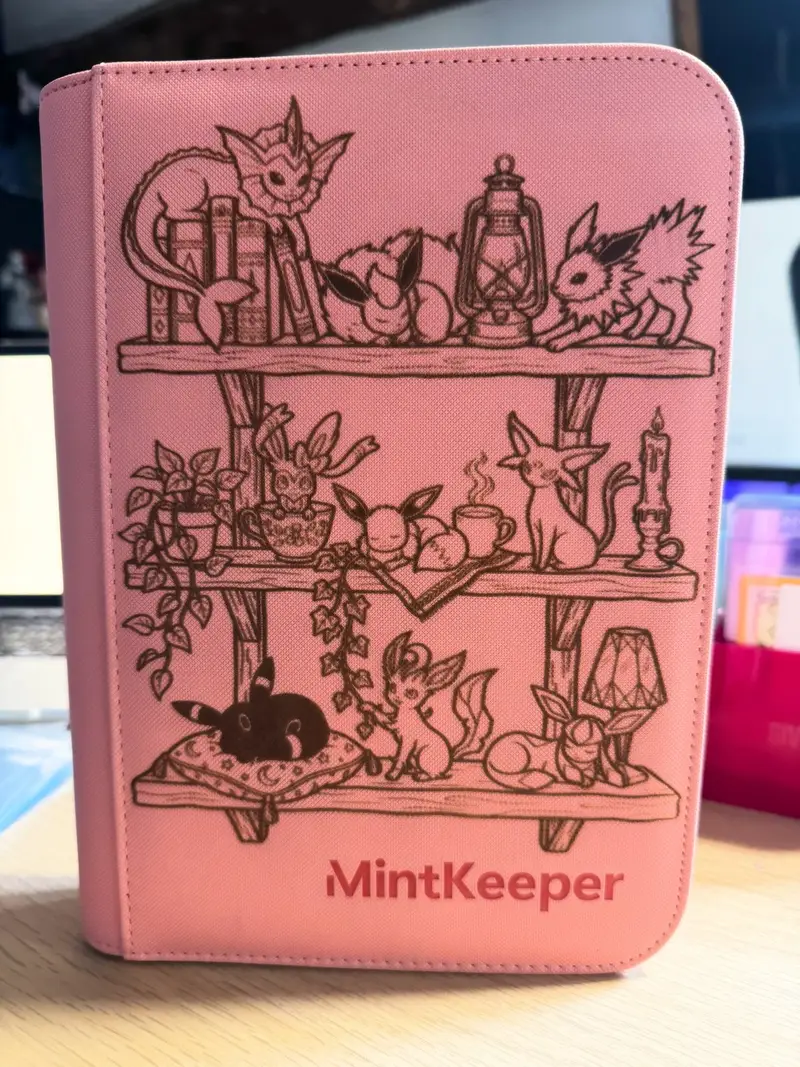 Black zip binder engraved in gold with a shelf of small Eeveelution-inspired figures and the title The Eevee Shelf.